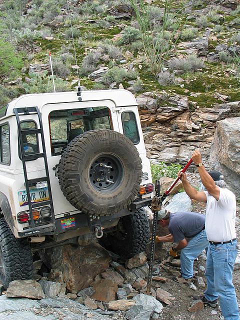 Leo jacks up his truck while Mike throws rocks under his wheel